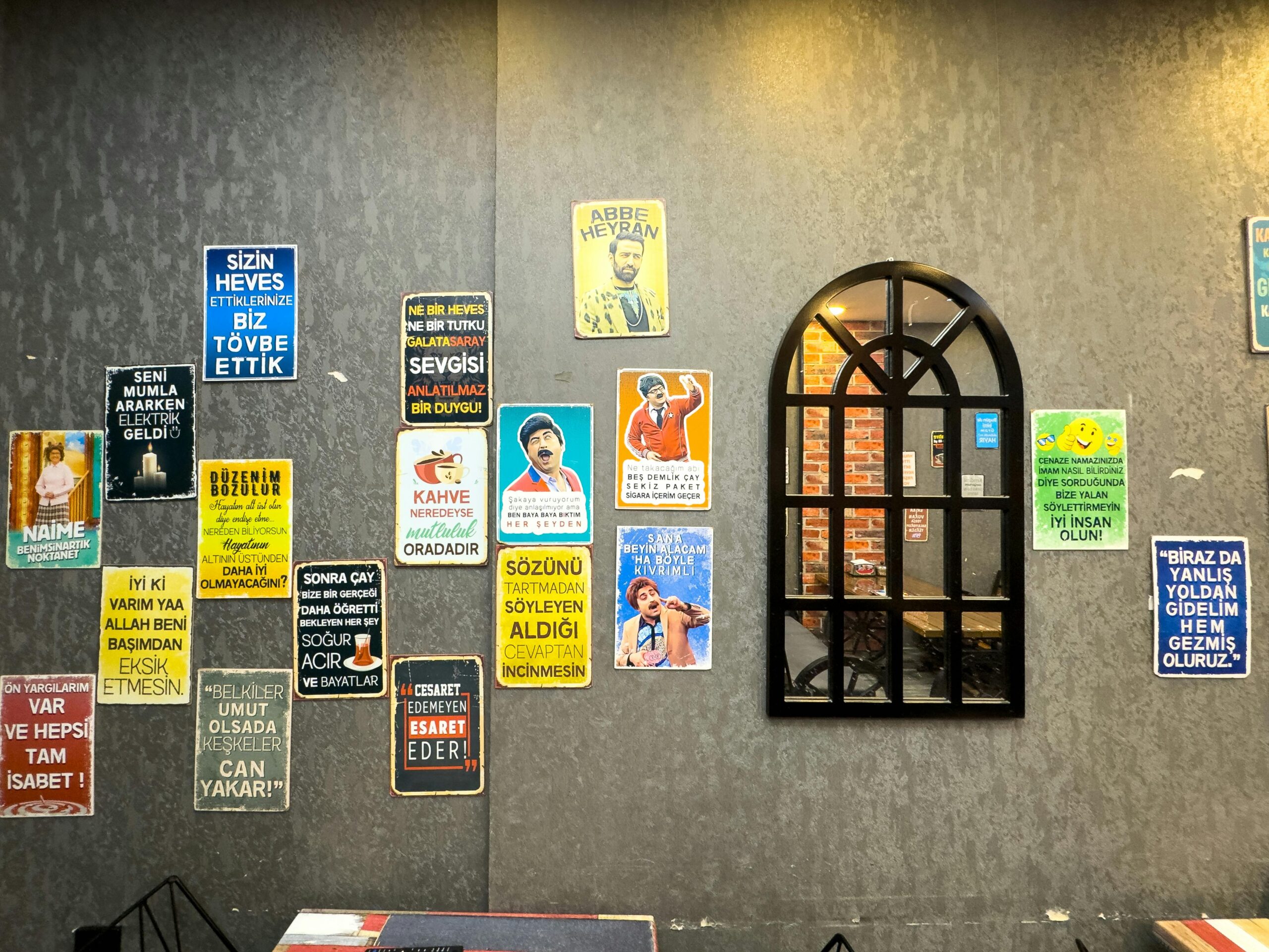 A wall adorned with colorful Turkish posters next to a reflecting mirror.